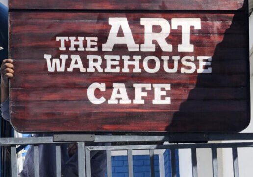 Image of a sign over a gate with The Art Warehouse cafe on it.