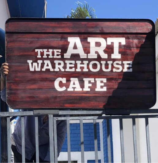 Image of a sign over a gate with The Art Warehouse cafe on it.
